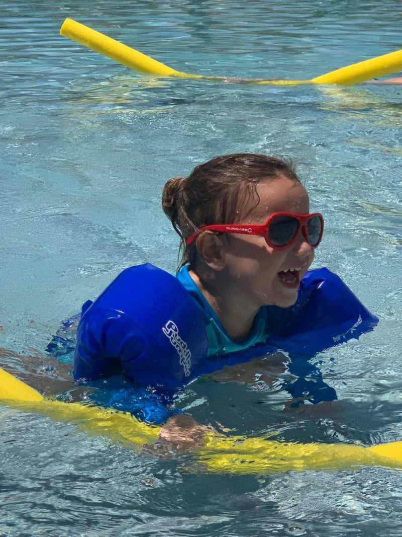 A young girl laughs and plays while wearing glasses in the pool