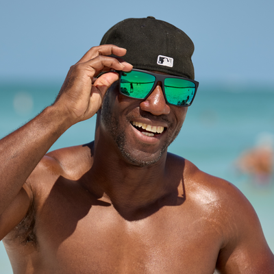 Man wearing a black cap and green sunglasses on a beach